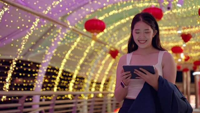 at night,young Asian woman happily plays with the tablet .She looks forward with hopes and dreams, a technology device of today in the middle of an urban society with buildings a in the backdrop.
