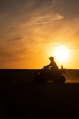 unrecognizable ATV driver in desert dunes at sunset