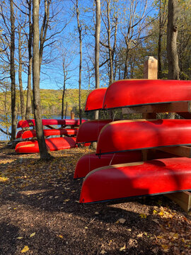 Canots rouges rang&eacute;s sur des supports de bois. For&ecirc;t en automne. Location d'embarcation nautique, cano&euml; de rivi&egrave;re, rabaska dans un parc national. Centre de plein air, p&ecirc;che et camping.