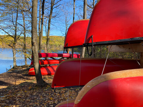 Canots rouges sur support en bois en for&ecirc;t &agrave; l'automne. Location d'embarcation nautique, cano&euml; de rivi&egrave;re, rabaska dans un parc national. Centre de plein air et de camping pr&egrave;s d'une rivi&egrave;re.