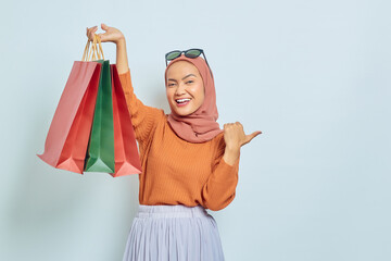 Smiling beautiful asian muslim woman in brown sweater and glasses showing shopping bags while...