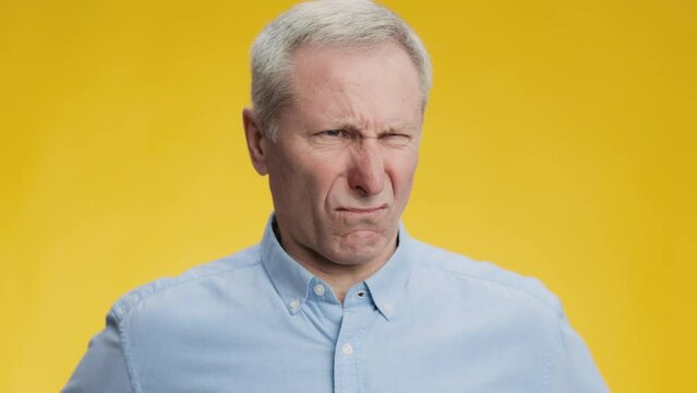 Eww. Portrait of disgusted senior man frowning nose, feeling awful stinky smell. yellow studio background, slow motion