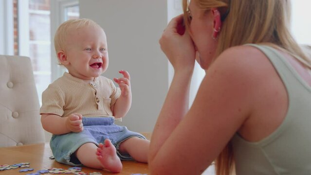 Mother And Baby Son Having Fun Sitting At Table At Home Playing Peek A Boo With Jigsaw Puzzle Pieces Together - Shot In Slow Motion