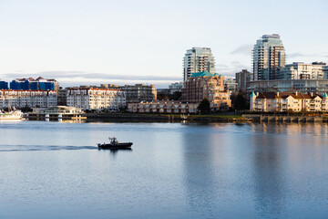 Obraz premium Small boat from the harbour patrol cruising along during a sunny early morning with buildings in the background, Victoria, British Columbia, Canada