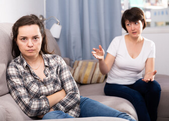 Sad young female and her elderly sister sitting at sofa during quarrel at home