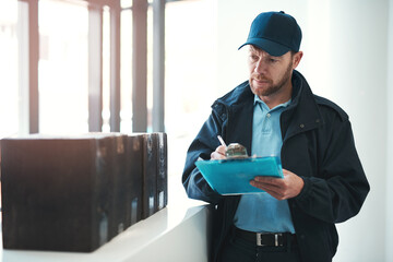 Making sure every delivery is signed and dated. Shot of a handsome delivery man writing on his clipboard while waiting in the lobby with a customers order.