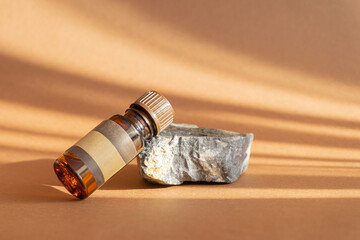 Concept of aromatherapy. Amber-colored jar, unmarked, with label, lies on stand made of natural granite stone. Rays of sunlight reflecting off oil container cast shadows on surface