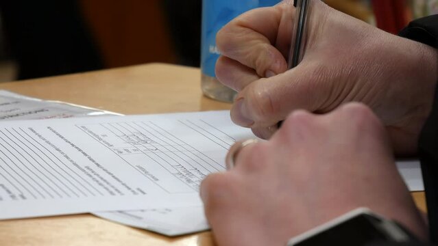 Close up of a  woman filling out a form on a reception desk. The female uses a pen to write her information on a piece of paper.