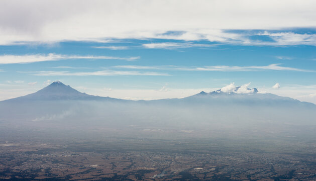 Panoramic view of the popocatepetl and Iztaccihuatl volcanoes during a summer day with cloudy blue sky - Powered by Adobe