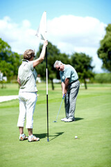 Master of the hole-in-one. A senior woman holding a flag while her husband puts for birdie.
