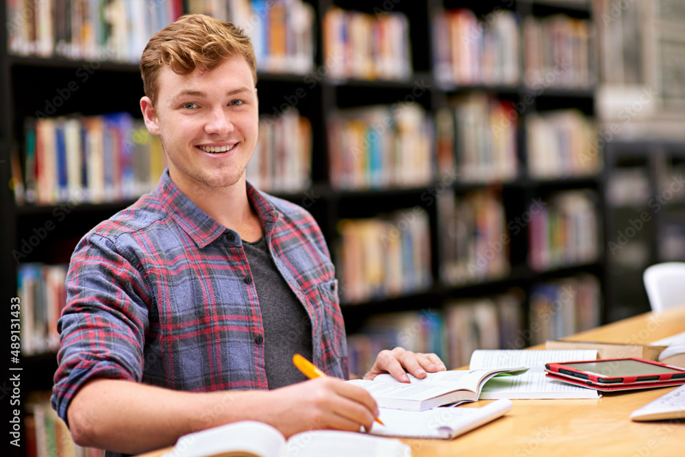 Poster hes top of his class. portrait of a male student studying at a table in a university library.
