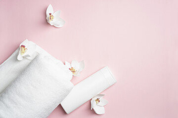 Fototapeta na wymiar White bottle of shampoo and hair conditioner on a pink background with a towel and orchid flowers. Exotic aroma mockup bathroom with copy space.