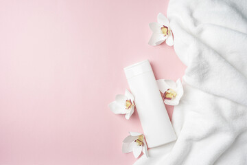Obraz na płótnie Canvas White bottle of shampoo and hair conditioner on a pink background with a towel and orchid flowers. Exotic aroma mockup bathroom with copy space.