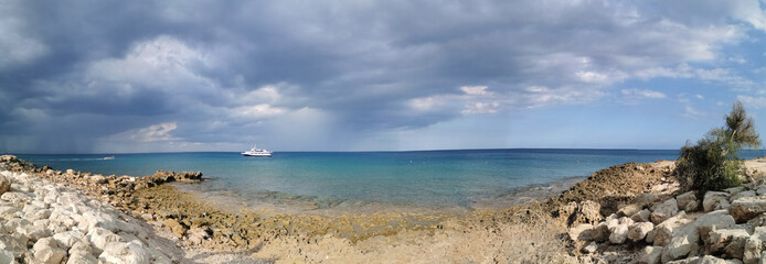 Panorama. The stone coast of the Mediterranean Sea, a white pleasure ship in the sea against a dramatic sky. with clouds.