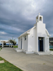 Fototapeta na wymiar The open white Chapel of St. Constantine and St. Helena on the seafront against a dramatic sky..flowering shrub on the streets of Protaras against a blue sky with clouds.