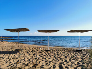 A small sandy beach on the Mediterranean Sea with three square parasols against a blue cloudless sky.