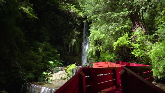 Waterfall streaming down near red wooden deck surrounded by woods in Termas Geometricas hot spring complex, Co&ntilde;aripe, Chile