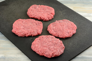 Raw formed ground beef hamburger patties on black cutting board