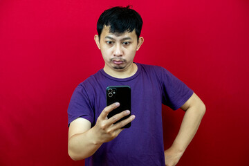 Asian man is looking at his smart phone with angry expression.