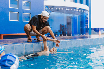 Latin swimming man trainer talking some advices to teenagers swimmers students at the pool in...