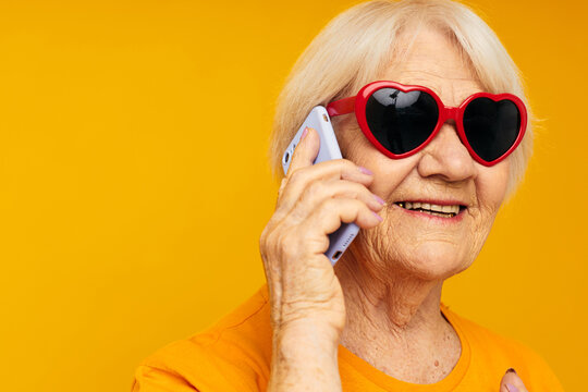 Portrait of an old friendly woman in dark glasses talking on the phone isolated background
