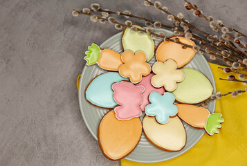Beautiful glazed Easter cookies on grey concrete background. Easter festive set of cookies and willow twigs. Holiday decorations. Colorful easter cookies on plate with yellow napkin.