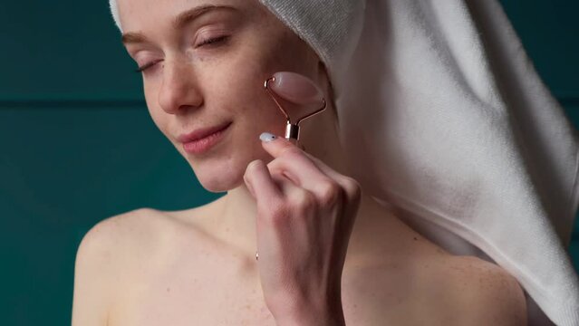 Freckled woman glowing skin using natural jade roller for facelifting rejuvenation face massage. Close-up portrait. Spa body care. Home concept. Rejuvenation