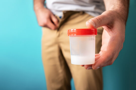 Fertility test. A man holds a jar of sperm in his hand. Close-up at the level of men's thighs. Blue background. The concept of sperm donation and artificial insemination