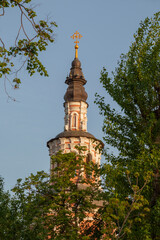 The bell tower of an old Orthodox church against the background of tree branches and blue sky