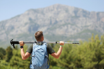 Athletic man with backpack and hiking sticks looks at mountain