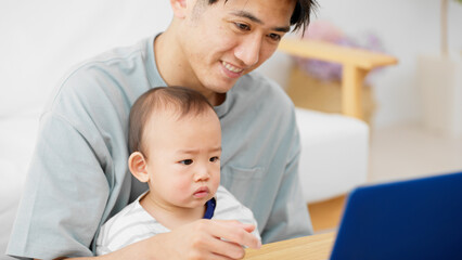 ノートパソコンを赤ちゃんに見せる父親