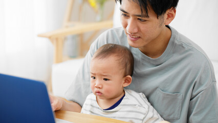 Fototapeta na wymiar ノートパソコンを赤ちゃんに見せる父親