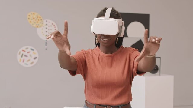 Medium slowmo shot of young African-American woman in vr headset gesticulating with her hands during virtual reality exhibition in modern art museum