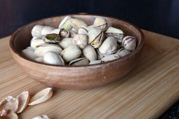 Pistachios in a wooden bowl on a wooden board. Dried nuts.