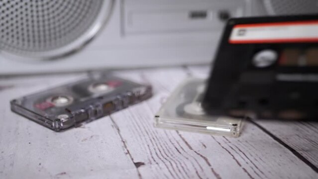 Female Hand Picks Up One Old Music Audio Cassette from the 90s from the Table. A pile of vintage magnetic tape cassettes lie on a table against the background of a stereo tape recorder. Nostalgia.