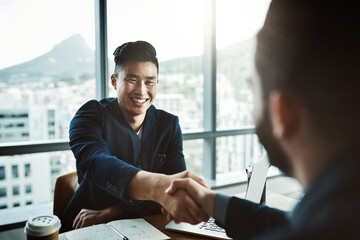Its safe to say he made a great impression. Shot of two young businessmen shaking hands while sitting at a desk in a modern office.