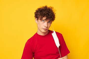 guy with red curly hair wearing a red t-shirt medical mask on the face posing yellow background unaltered