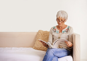 Getting in some peaceful reading. Shot of a senior woman reading a book while sitting on a sofa.