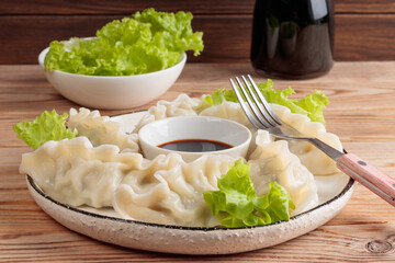 Close-up view of fresh boiled Chinese dumplings on rustic plate with soy sauce and green salad on wooden background. Selective focus.