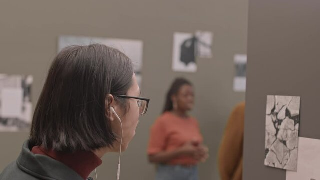 Medium close-up with slowmo of young Caucasian man using headphones while listening audio guide at photo exhibition in modern art gallery