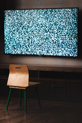 A small child chair in front of a tv with a white noise on the screen. Scary dark creepy horror unsaturated image