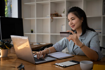 Young asian woman office worker holding credit card and shopping online on computer laptop.