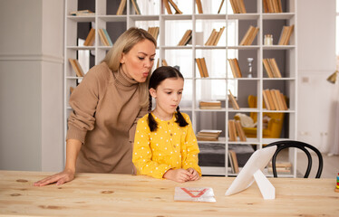 a speech therapist teacher is engaged with a schoolgirl girl at a table in a room. Correct pronunciation training