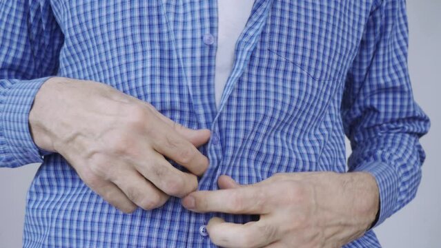 An elderly man struggles to button his clothes