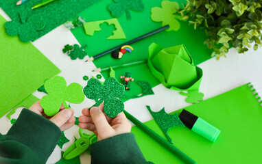 DIY St.Patricks Day decor. Top view a boy holding shamrocks craft card of shiny green paper....