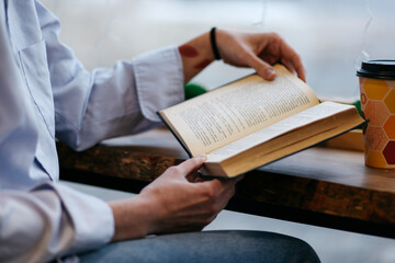 brunette girl in a cafe drinking coffee, reading a book, close up
