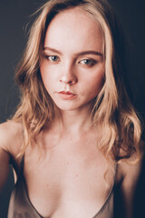 Fototapeta premium Young girl with a European Slavic appearance and brown hair, in a beige chemise, a dress with straps, playfully looks at the camera, acting skills and simple facial expressions on her face
