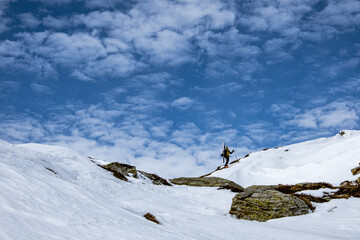 Alpinista in salita con sci a spalla tra neve e rocce, Valserhorn - Rheinwald, Grigioni, Svizzera