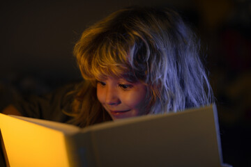 Child reading a book in bed before going to sleep. Little boy lying on bed reading book at home....