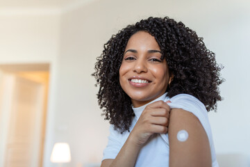 Portrait of a female smiling after getting a vaccine. Woman holding down her shirt sleeve and...